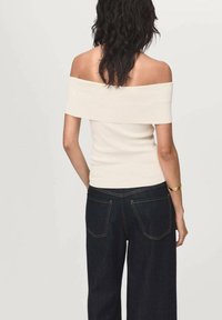 Crème top met schoudervulling, gemaakt van stretchstof, met een aansluitend ontwerp, gedragen met donkere, wijde jeans met achterzakken en gele stiksels.
