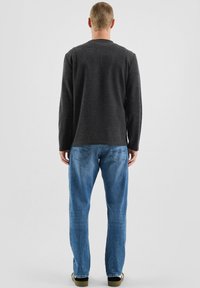 Długo rękawem ciemnoszara koszula z okrągłym dekoltem, w połączeniu z jasnoniebieskimi dżinsami. Charakteryzuje się luźnym krojem i gładką fakturą.