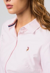 Lichtroze gestreepte blouse met een klassieke kraag. Bevat een klein geborduurd accent en een decoratieve detail aan de binnenkant van de kraag in marineblauw en rood.