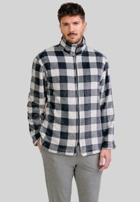 Chaqueta de forro polar con un patrón de cuadros en blanco y negro, con un cuello alto y cierre de cremallera completa. Textura suave y mangas largas.