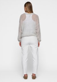 Hellegrauer, strukturierter Pullover mit transparenten Rückendetails, kombiniert mit weißen, schmal geschnittenen Hosen und braunen, kuscheligen Slip-On-Schuhen.