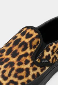 Slip-on Vans tenisice s uzorkom leoparda, crnom gumom na potplatu i elastičnim bočnim detaljima. Teksturirani materijal s toplim smeškim i crnim mrljama.