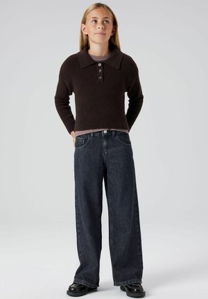 Bruine geribde trui met een brede kraag en drie knopen. Gecombineerd met losse donkere jeans en zwarte schoenen. Schoon, minimalistisch ontwerp.