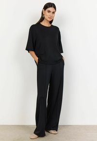 Top oversized de culoare neagră cu mâneci scurte, purtat cu pantaloni largi negri. Material neted, cu o croială lejeră și buzunare laterale, completat cu pantofi ușori.