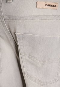 Ljusgrå denimjeans med en bakficka, stickade detaljer och en läderetikett som står "DIESEL" nära midjan.