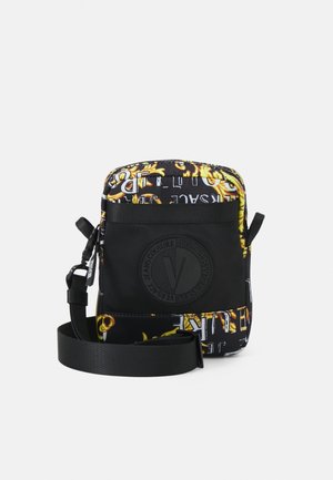 Sort Versace crossbody taske med gult barokmønster, logo foran og justerbar rem på hvid baggrund.