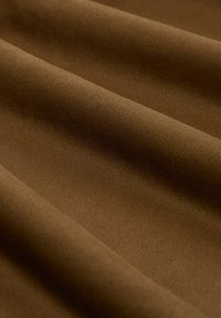 Tessuto marrone con una texture liscia, caratterizzato da drappeggi piegati che evidenziano il suo colore ricco e la leggera lucentezza. Probabile miscela di cotone o poliestere.