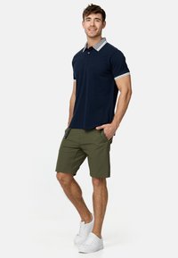 Marineblå polo-shirt med mønstret grå krave og hvide detaljer, parret med olivengrønne shorts og hvide sneakers, alt sammen tætsiddende og afslappet.
