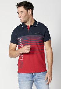 Polo tričko s červenými a námorníckymi pruhmi má golier, krátke rukávy a logo. Vyrobené z bavlny pre pohodlie a priedušnosť.