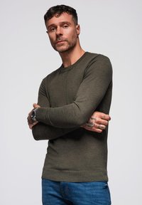 Maglione lungo a maniche lunghe di colore verde oliva, con un design aderente, realizzato in morbido tessuto a maglia. Il maglione presenta un colletto tondo e polsini a coste.