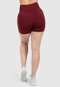 Pantaloni corti bordeaux a vita alta realizzati in un tessuto elasticizzato con una trama liscia. Presentano un design aderente e un dettaglio a cucitura arrotondata sul retro.