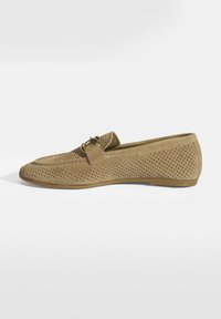 Hellbraune Wildleder-Loafers mit perforiertem Design, flacher Gummisohle und einem kleinen dekorativen Hardware-Detail am Riemen.