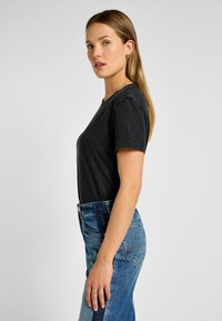 T-shirt nera in cotone con maniche corte, scollatura rotonda e vestibilità rilassata, abbinata a jeans in denim blu a vita alta.