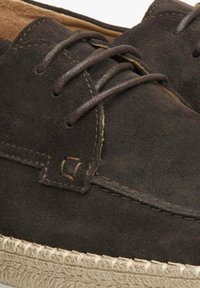 Hnědé semišové boty s texturovaným povrchem, které mají tmavé šněrování, prošívané detaily a pletenou jutu podrážku.