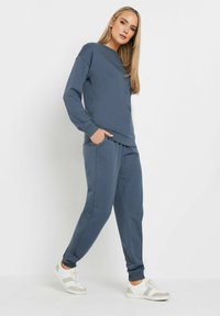 Sudadera gris y joggers a juego hechos de material suave, con un ajuste holgado, mangas largas y bolsillos laterales. Zapatillas blancas completan el look.