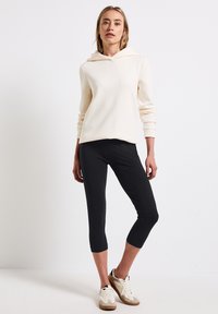 Huvtröja i krämfärg med långa ärmar, kombinerad med svarta capribyxor och vita sneakers med beige detaljer. Minimalistisk design.