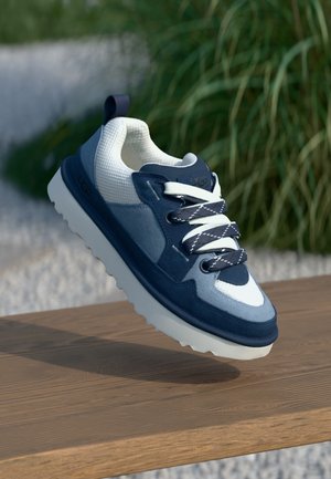 Blue and white sneaker with a mesh upper, suede accents, round laces, and a chunky white sole, suspended above a wooden surface.