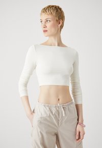 Top scurt alb, ajustat, cu mâneci lungi și gât larg tip barcă. Asortat cu pantaloni cargo bej deschis. Textură netedă.