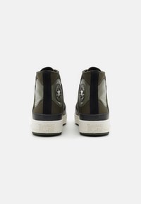 Para oliwkowych i czarnych sneakersów Converse All Star typu high-top widocznych z tyłu na białym tle.