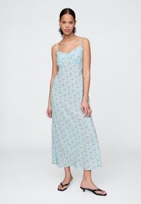 Svetlo modra cvetna obleka z tanjšimi naramnicami, dolžine do polovice meč, z nagubanim zgornjim delom in majhnimi rdečimi in rožnatimi cvetličnimi vzorci povsod.