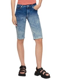 Denim shorts in een vervaagd blauw verloop, knielang met een ruwe zoom, gecombineerd met zwarte enkelband sandalen met een dikke zool.