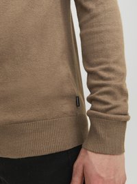 Brauner Strickpullover mit gerippten Bündchen und Saum, aus einem weichen Material gefertigt. Verfügt über ein kleines Etikett an der Seite.