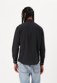 Svart langermet skjorte med krage, knapper på mansjettene og en glatt tekstur, båret med lyseblå jeans.