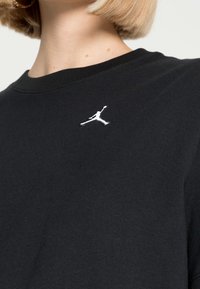 Sort bomulds t-shirt med rund halsudskæring, prydet med et lille hvidt Jordan-logo broderet på venstre brystområde. Glat tekstur.