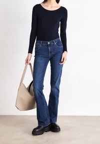 Navy long-sleeve top, slim-fit, with round neckline, paired with dark blue flared jeans; model holds a beige tote bag; black platform boots.