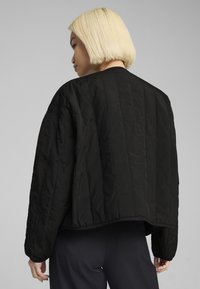 Schwarze gesteppte Jacke mit lockerer Passform, abgerundetem Saum und langen Ärmeln. Hergestellt aus strukturiertem Stoff mit feinen Nähten.