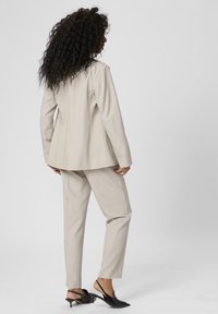 Světlý béžový oblek s šitým sakem a úzkými kalhotami. Doplněno o elegantní černé lodičky, které zdůrazňují ostré linie outfitu.