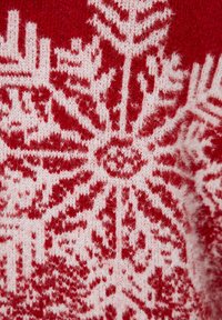 Punainen ja valkoinen neulottu kangas, jossa on lumihiutaleiden kuviointi hienolla yksityiskohdalla. Rakenne näyttää pehmeältä ja pörröiseltä, mikä tekee siitä sopivan talvivaatteisiin.