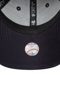 Interior de una gorra de béisbol negra con visera curvada, que presenta una pegatina holográfica plateada de una pelota de béisbol y un forro de malla.