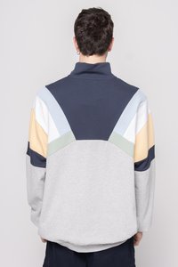 Grå fleece genser med fargeblokkerte detaljer på ryggen i marineblått, lyseblått, blekgult og grønt. Høy krage, avslappet passform, myk tekstur.