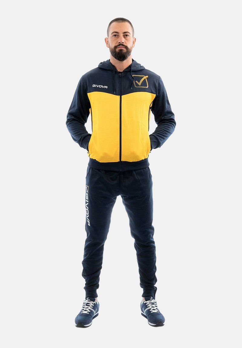 Set di abbigliamento sportivo composto da una giacca con zip di colore blu navy con accenti gialli e pantaloni coordinati, entrambi realizzati in un morbido tessuto testurizzato.