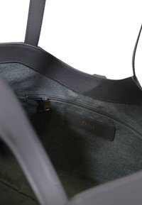 Borsa tote in pelle grigia con interni in tessuto. Presenta una tasca con zip e un'etichetta, evidenziando texture lisce e linee pulite.