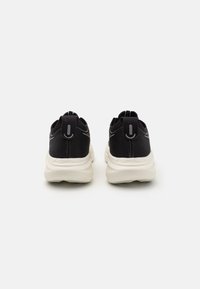 Baskets de sport noires avec un tissu texturé et des semelles de couleur claire. Les caractéristiques incluent un talon rembourré et des accents réfléchissants sur le dessus.