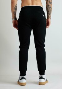 Czarne spodnie dresowe wykonane z miękkiego materiału, o dopasowanym kroju, z prążkowanymi mankietami oraz tylną kieszenią z małym detalem w postaci logo.