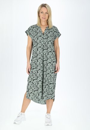 Robe à boutons florale noire avec des fleurs vert pâle, à manches courtes et fentes sur les côtés, associée à des baskets blanches.