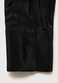 Poignet de chemise en satin noir avec un seul bouton noir cousu près du centre sur un fond de tissu lisse.