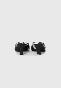 Mules avec motif vache noir et blanc, dotées d'un dessus en tissu lisse, d'un dos ouvert et d'un talon moyen à bloc, avec une semelle extérieure noire mate.