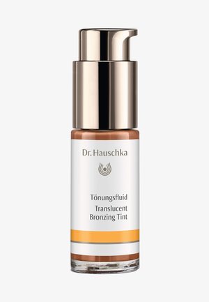 Dr. Hauschka Translucent Bronzing Tint in einer klaren Glasflasche mit einem goldenen Pumpverschluss, versehen mit weißen und orangen Markierungsdetails.
