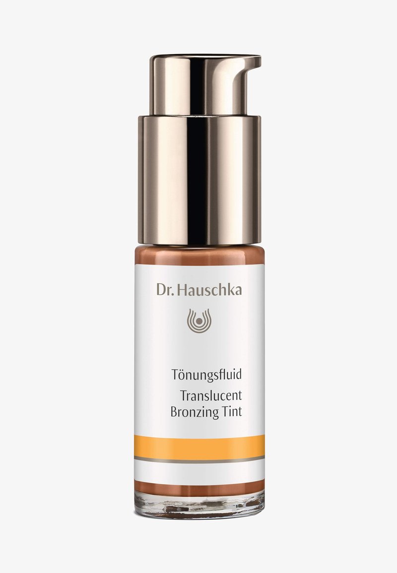 Il Tinta Abbronzante Traslucido di Dr. Hauschka è contenuto in una bottiglia di vetro trasparente con un tappo a pompa dorato, caratterizzato da dettagli di branding bianchi e arancioni.