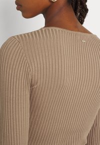 Ribbed brown top with a textured finish, featuring a round neckline and a small logo tag at the back, highlighting a fitted design.