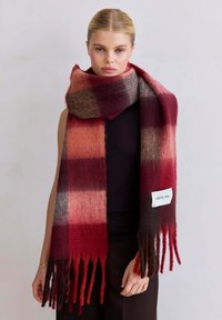 Écharpe à carreaux dans des nuances de rouge, bourgogne et gris. Fabriquée en matériau doux avec des bords à franges. Une étiquette sur un côté indique "ARCTIC FOX."