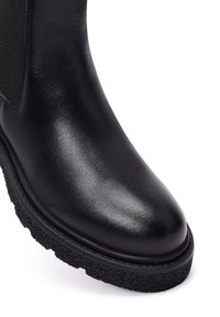 Czarny botek sięgający kostki z gładkiej, błyszczącej skórzanej cholewce, elastycznymi panelami bocznymi oraz teksturowaną czarną gumową podeszwą. Okrągły kształt palców.