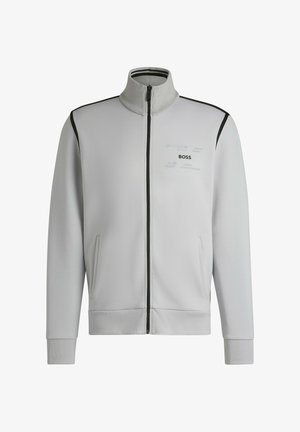 Vaaleanharmaa vetoketjullinen takki, jossa on korkea kaulus, kaksi sivutaskua, mustat korostukset ja hillitty logo rinnassa. Pehmeä kangas.