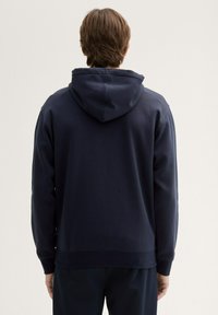 Granatowy hoodie wykonany z miękkiego materiału, z dużym kapturem, ściągaczami przy mankietach i u dołu. Brak widocznych logo lub wzorów, gładka faktura.