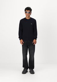 Σκούφος ναυτικού στιλ με ριμπ μανσέτες, συνδυασμένος με μαύρα τζιν στο χαλαρό στιλ και σκούρα αθλητικά παπούτσια. Αξεσουάρ περιλαμβάνουν ανακλαστικά γυαλιά ηλίου.