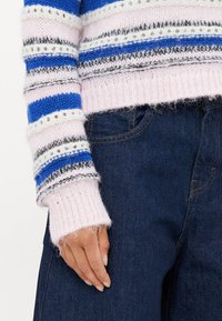Stripet strikkegenser i blå, rosa og grå farger; myk tekstur; løst snitt; lange ermer med ribbestrikkede mansjetter; brukt over mørke denimjeans.